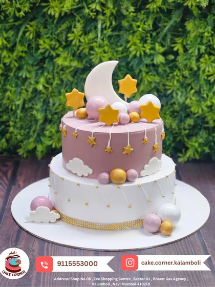 A dreamy two-tier cake with a moon and stars theme. The pastel pink and white colours, along with the golden stars, create a magical and serene look.