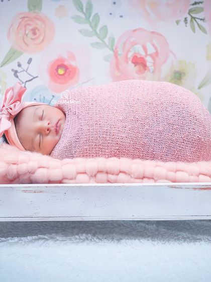 A beautiful composition with a floral wallpaper backdrop. The baby is swaddled in pink and sleeping on a miniature white bed.