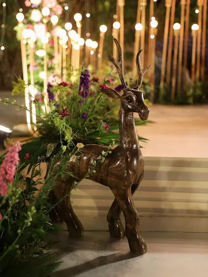 A whimsical decor element featuring a wooden deer statue adorned with fresh flowers. This piece adds a touch of enchanted forest magic to the event space.