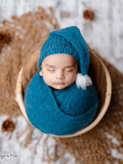 A perfectly posed newborn portrait. The baby boy is swaddled in blue and nestled in a wooden bowl, creating a sweet and artistic image.