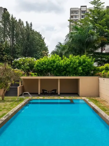 This view shows the semi-covered seating pavilion at the end of the pool. This structure provides a shaded space for relaxation and is integrated into the landscape with surrounding trees and a lawn, making it feel like a natural extension of the garden.