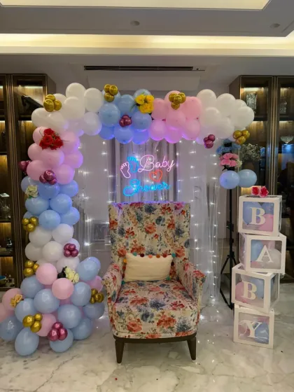 An elegant "Oh Baby" shower setup featuring a floral armchair for the mom-to-be. The pastel balloon arch, fairy light curtain, and "BABY" blocks create a sophisticated and comfortable setting.
