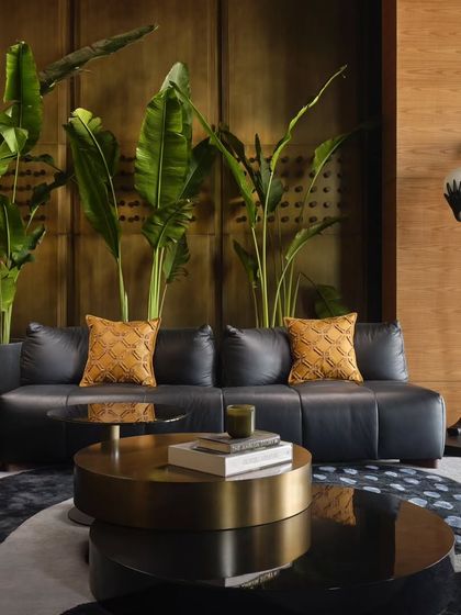 A close up of the lounge, highlighting the mix of textures. The smooth leather of the sofa contrasts with the warm brass wall, while large tropical plants add a touch of life and color, creating a multi-sensory experience.