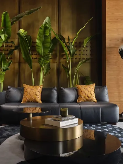 A close up of the lounge, highlighting the mix of textures. The smooth leather of the sofa contrasts with the warm brass wall, while large tropical plants add a touch of life and color, creating a multi-sensory experience.