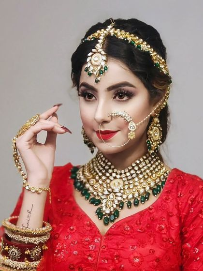 A bride in a red lehenga wearing a Kundan and emerald jewellery set. The hathphool and bangles complete the traditional look.