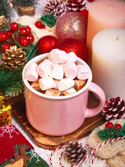 A cozy mug of hot chocolate topped with marshmallows, surrounded by warm Christmas decorations and candles. This image perfectly captures the comforting spirit of the holidays.