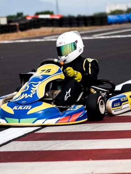 A driver in the number 75 kart, perfectly positioned on the red and white kerb.
