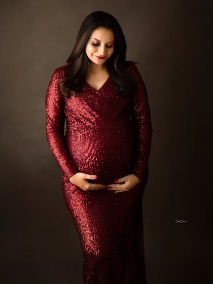 A quiet moment of connection. This mom-to-be looks down at her bump, dressed in a glamorous, floor-length red sequin gown.