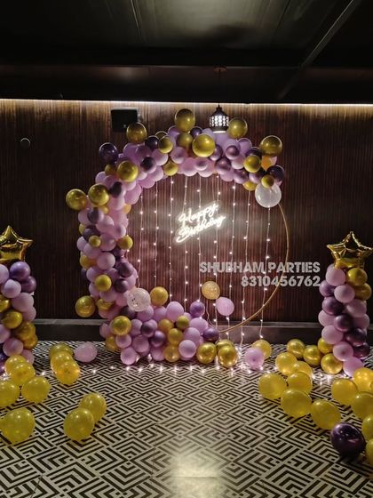 A purple and gold balloon ring with fairy lights, set up for a birthday party in a dimly lit venue.