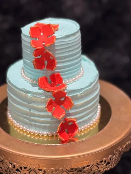 A chic and modern mini two-tier cake in a beautiful teal color. The cake is adorned with red monstera leaf accents and pearl borders, perfect for a stylish New Year's event.