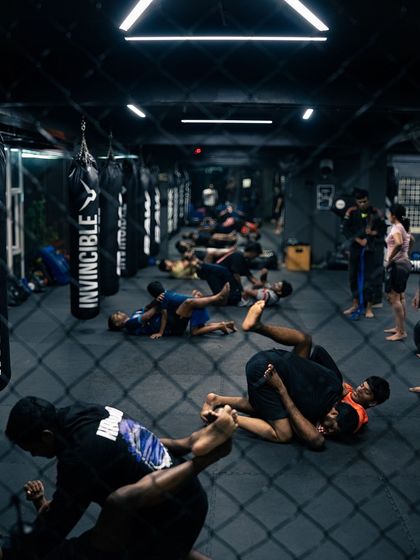 An overhead view of the mat during a Jiu-Jitsu class, showing multiple pairs of students grappling.
