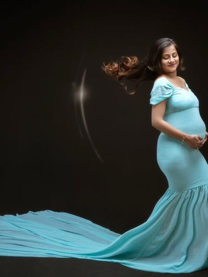 In this serene moment, our beautiful mumma-to-be is lost in thought, gently cradling her precious baby bump in a flowing sea-blue gown.