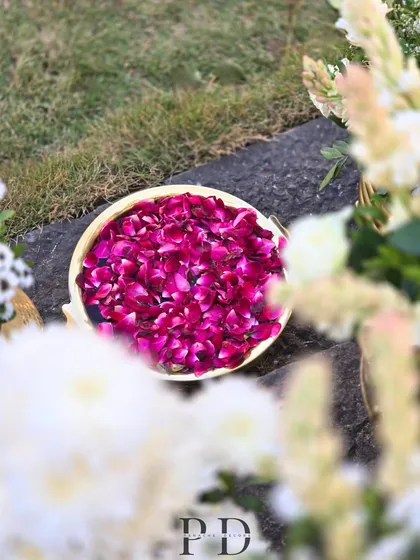 A bowl of vibrant pink rose petals, ready for showering the couple, set amidst other floral and brass decor elements.
