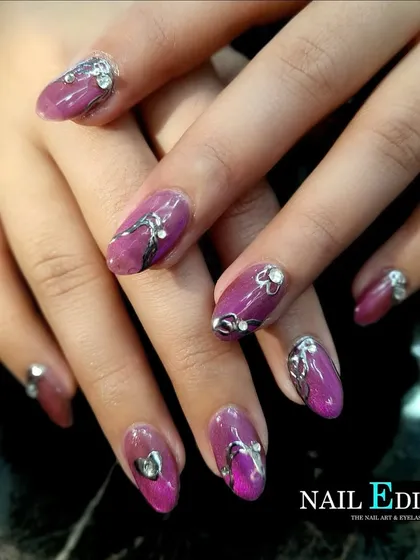 This manicure features a rich magenta base with sculpted silver chrome accents and sparkling rhinestones. The combination of chrome and gems creates a bold and luxurious design.