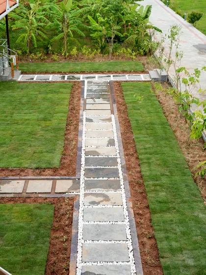 An aerial view of a formal garden layout, with a central stone pathway bordered by white pebbles and flanked by symmetrical lawns.