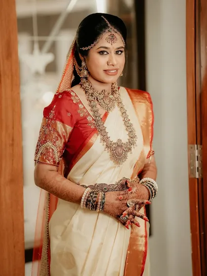 A full-length portrait of the bride in her beautiful off-white and red silk saree, showcasing her complete traditional Muhurtham look.