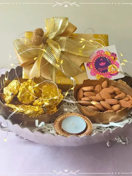 A silver-finish urli filled with chocolates, almonds, and a T-light, wrapped with fairy lights. This shows how a traditional urli can be used to create a modern and beautiful gift hamper.