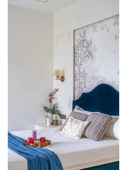 A detailed shot of the bedside, highlighting the rich blue velvet headboard, delicate floral wallpaper, and elegant wall sconce. Every detail is chosen to contribute to a serene atmosphere.