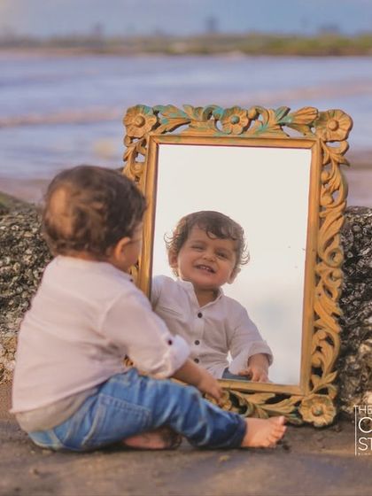 Who is that handsome boy in the mirror? A moment of sweet discovery for this little one on the beach, as he gazes at his own smiling reflection.