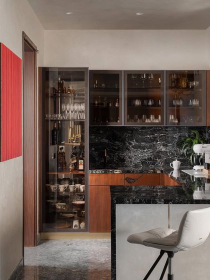 The dry kitchen and bar area features a striking black marble backsplash and countertop. Glass-fronted cabinets display glassware, while a bold red art piece adds a pop of color, making this transitional space a design feature in its own right.