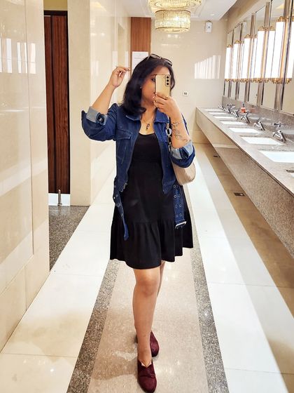 A mirror selfie in a washroom, a classic way to capture your outfit of the day. The denim jacket and black dress combo is effortlessly cool.