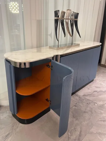 This elegant sideboard features a white marble top and a body finished in a dusty blue Duco paint. The fluted, curved doors and chrome accents give it a sophisticated, Art Deco feel.