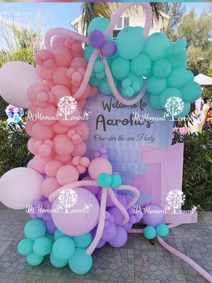 A welcome sign for Aarohi's "One-der the sea" party. The sign is framed by an elaborate arrangement of pink, purple, and teal balloons, creating a beautiful first impression.