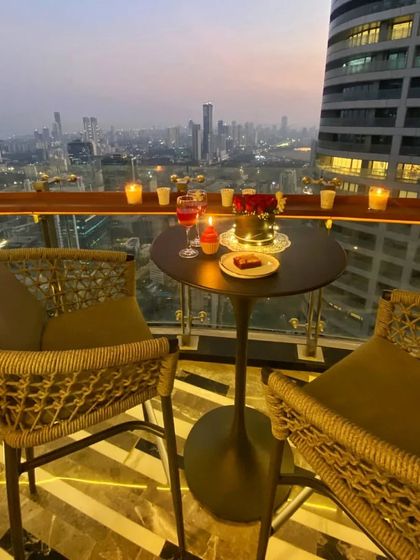 A romantic dinner for two on a high-rise balcony. The wicker chairs add a touch of natural texture, creating a cozy and intimate setting to enjoy the city view.