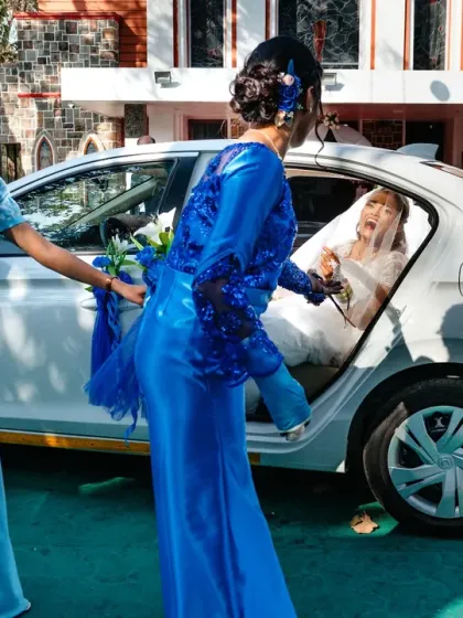 A candid moment of the bridesmaids helping the bride out of the wedding car.