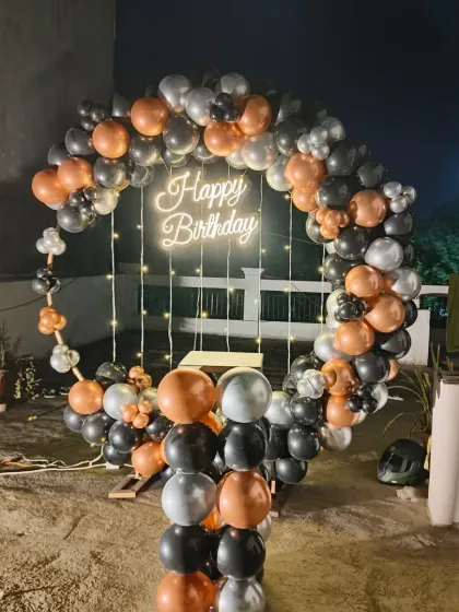 A stylish outdoor balloon ring for a terrace party. The black, copper, and silver balloons create a chic and modern look against the night sky.