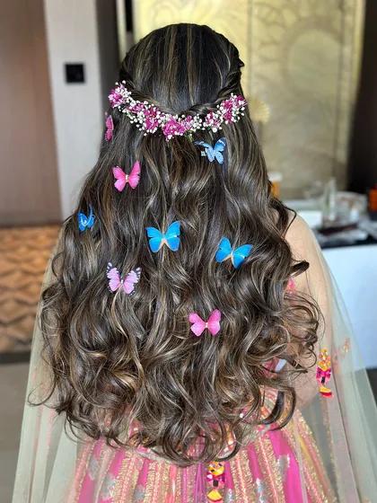 Fluttering elegance. This half-up style features a floral braid crown and a cascade of soft curls dotted with colorful butterflies.