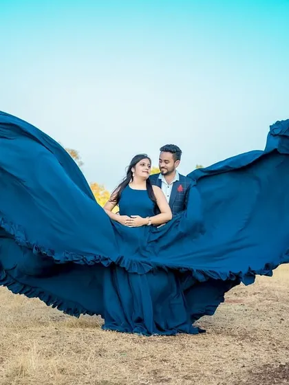 A dramatic "flying gown" shot in an open field. The deep blue fabric creates a stunning contrast against the bright blue sky.