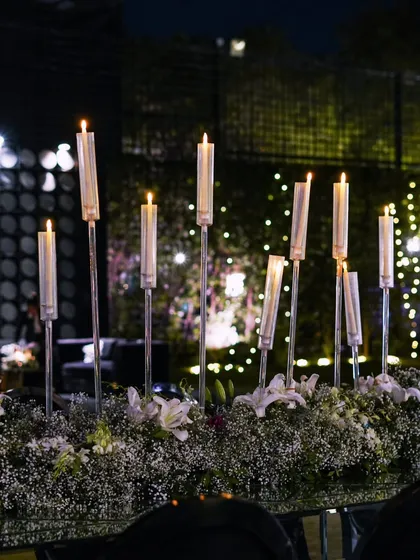 A beautiful tablescape featuring tall, elegant candle stands amidst a bed of baby's breath and white lilies, set against the sparkling backdrop of the event.