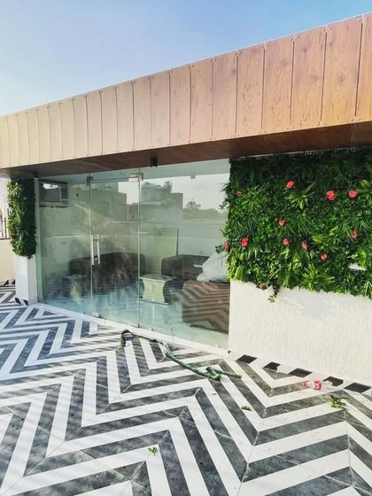 The entrance to a terrace lounge area, framed by artificial green walls with pink flowers. The bold black-and-white chevron floor tiling provides a striking contrast.