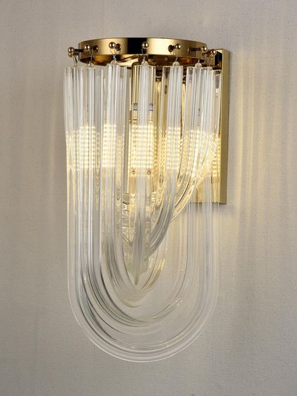 A close-up of the curved glass tube wall sconce. The quality of the glass and the warm light create a luxurious feel.