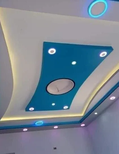 A modern, curved design using a bold blue accent color. The cove lighting follows the curves, and the multiple spotlights ensure the room is well-lit.