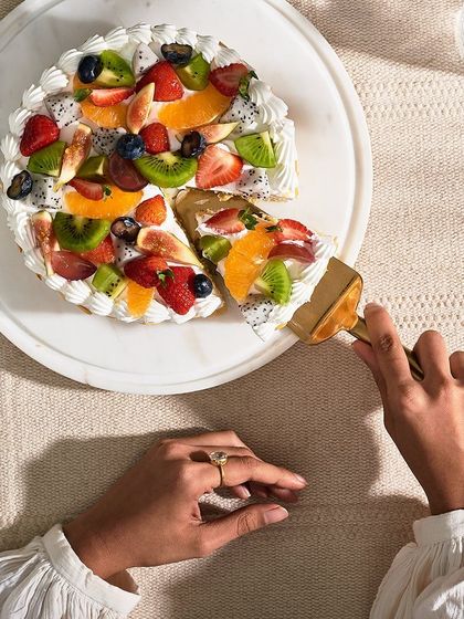 An overhead view of someone taking the first slice of the Fresh Fruit Gateau. The colorful arrangement of fruits makes it look like a jewel box.