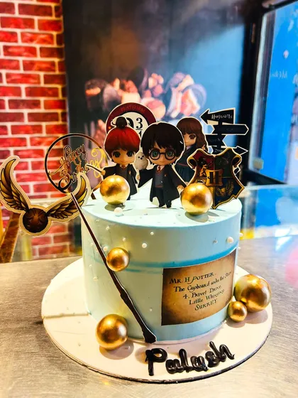 A magical Harry Potter-themed cake featuring chibi versions of Harry, Ron, and Hermione, a golden snitch, and a wand.