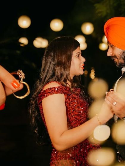 A creative shot focusing on the engagement ring held in the foreground, with the couple dancing romantically in the softly lit background.