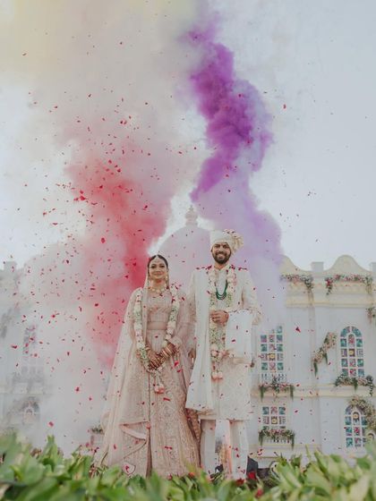 A dramatic and celebratory portrait of the couple with colored smoke and a shower of petals. This vibrant and energetic shot perfectly captures the excitement of their wedding day.
