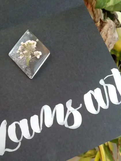 A diamond shaped pendant with a small pink and white flower, perfect for everyday wear.