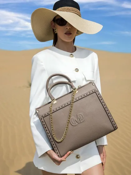 A high-fashion shot from the Da Milano desert campaign. The model wears a vintage-inspired white suit and a large sun hat, creating a look of timeless glamour that perfectly complements the sophisticated leather tote.
