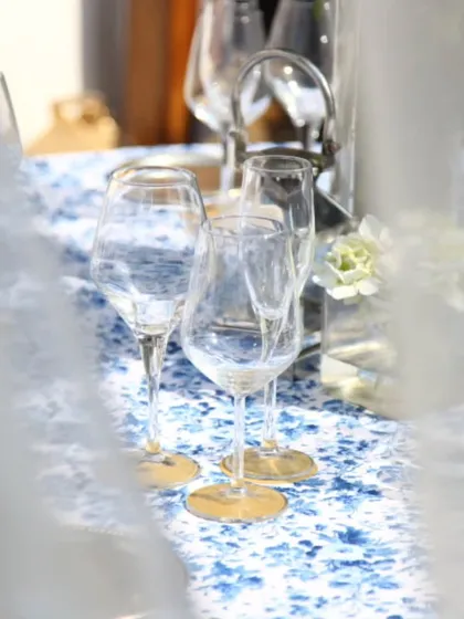 A dreamy, light-filled table setting with delicate glassware and a blue floral runner. This artistic shot captures the romantic and enchanting atmosphere we strive to create.