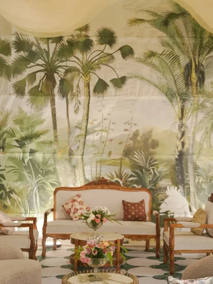 A serene Nikaah seating area. The vintage-style ivory sofa and chairs with intricate wooden frames are set against a lush, hand-illustrated palm backdrop, creating a timeless and intimate feel.