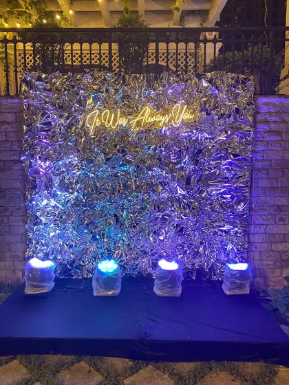 This modern and romantic photo booth was designed for a sangeet night. The shimmering silver foil backdrop and the warm glow of the "It Was Always You" neon sign create a perfect, intimate spot for couples' photos.