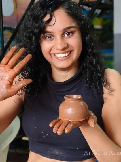 A student waves with a clay-covered hand while holding her first pot. The joy and pride in our students' faces are what our workshops are all about.