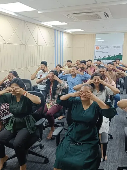 Participants cover their eyes during a palming exercise in a corporate session. This yogic technique helps to soothe tired eyes from screen fatigue and brings a sense of deep relaxation to the mind.