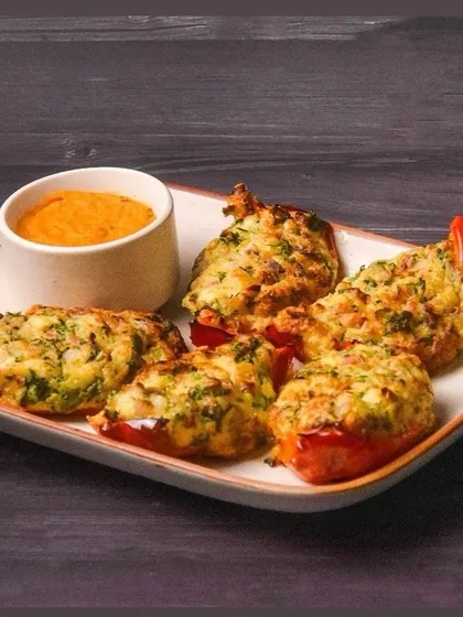 A platter of stuffed bell peppers with a side of peri-peri hummus. The dark, moody lighting highlights the texture of the filling and the roasted peppers.