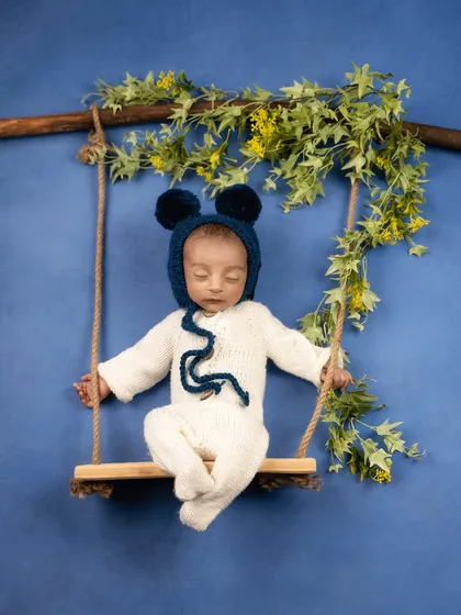 A variation of the swing setup, this time with the baby wearing an adorable bear-ear bonnet. The deep blue background makes the white outfit pop.