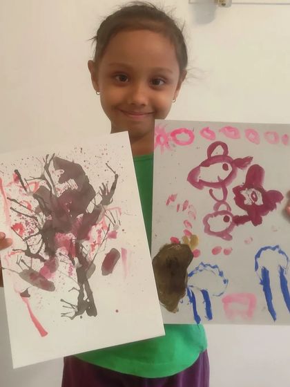 A student displays two of her creations, including an abstract cherry blossom tree made with the straw-blowing technique.